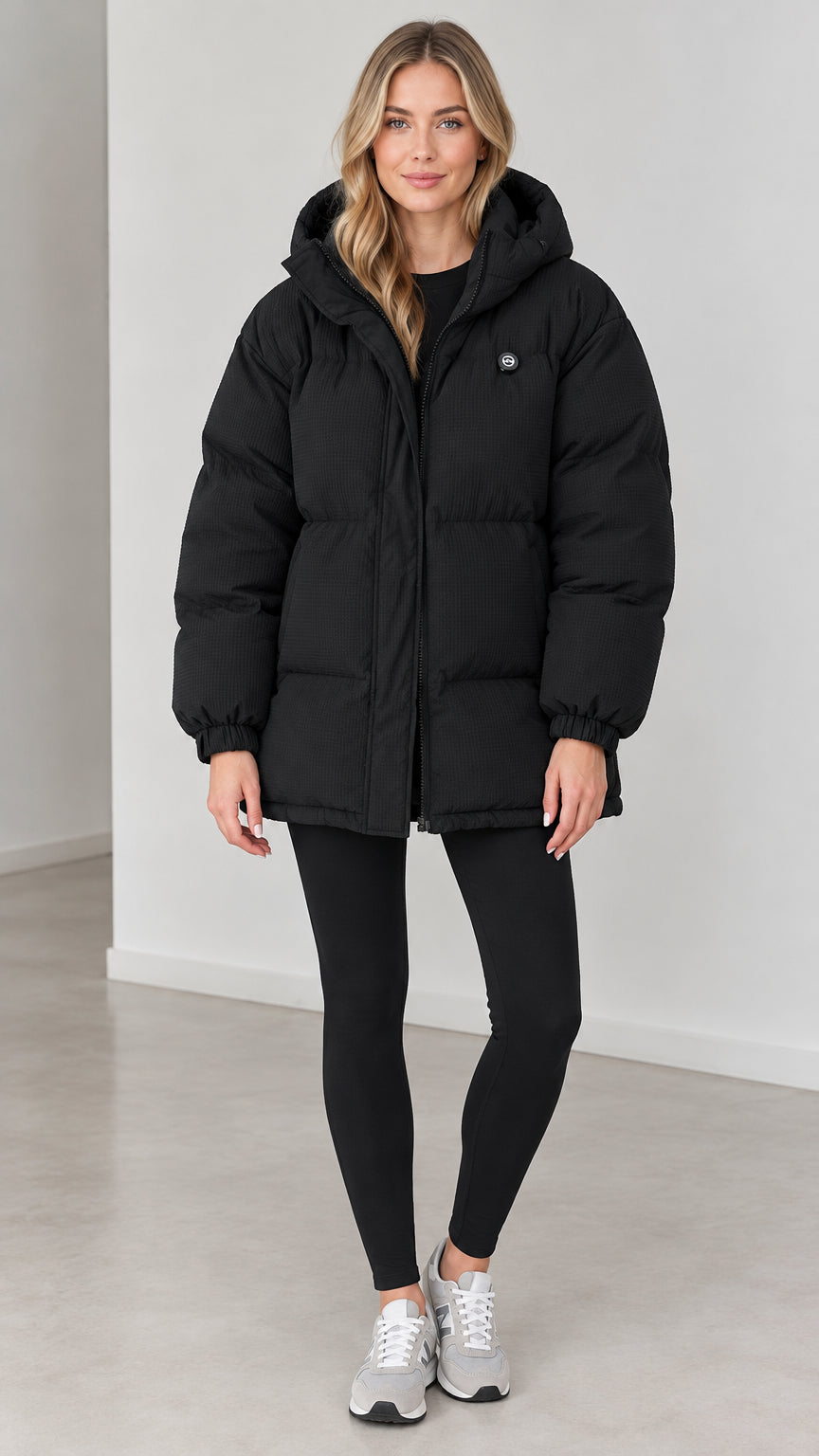 Front view of woman wearing black hooded oversized puffer jacket with leggings and sneakers