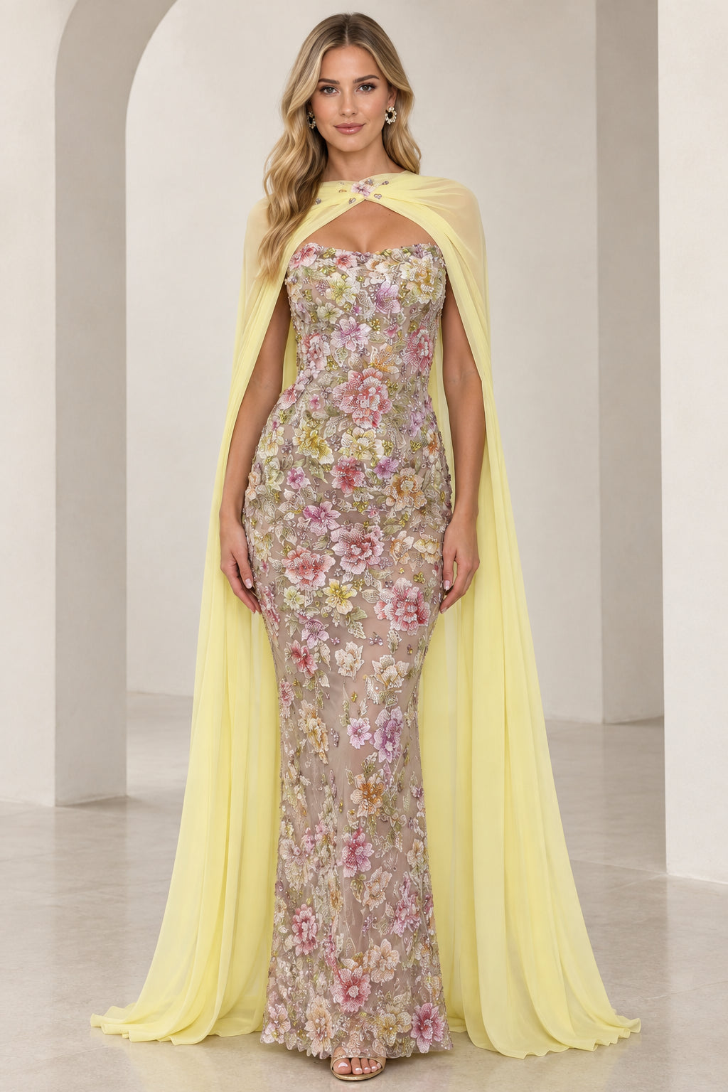 Front view of model wearing yellow floral embroidered strapless evening gown with matching sheer cape