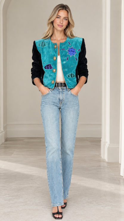 Model wearing teal celestial applique cropped jacket with black velvet sleeves and light wash jeans front view