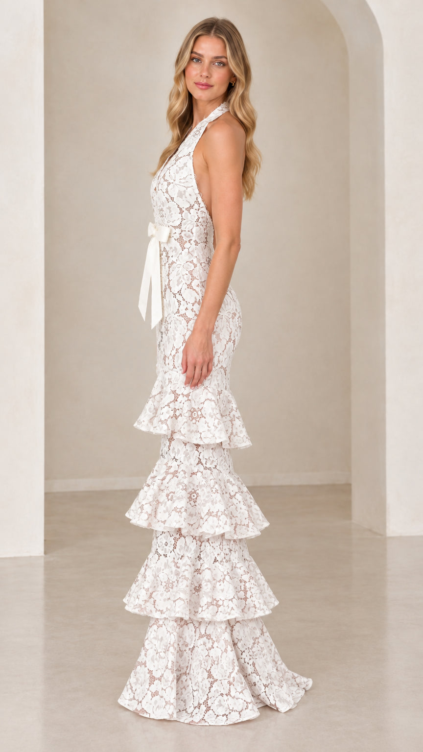 Side profile of model wearing White halter floral lace gown with tiered ruffle skirt
