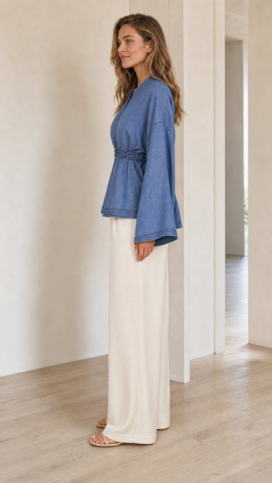 Side profile view of woman wearing denim blue bell sleeve tunic top with cinched waist