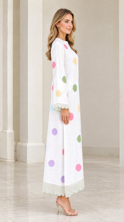 Side profile of woman in white polka dot maxi dress with scalloped hem
