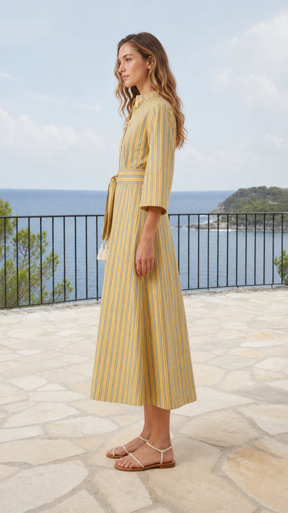 Side profile of model wearing yellow striped A-line midi dress on seaside balcony