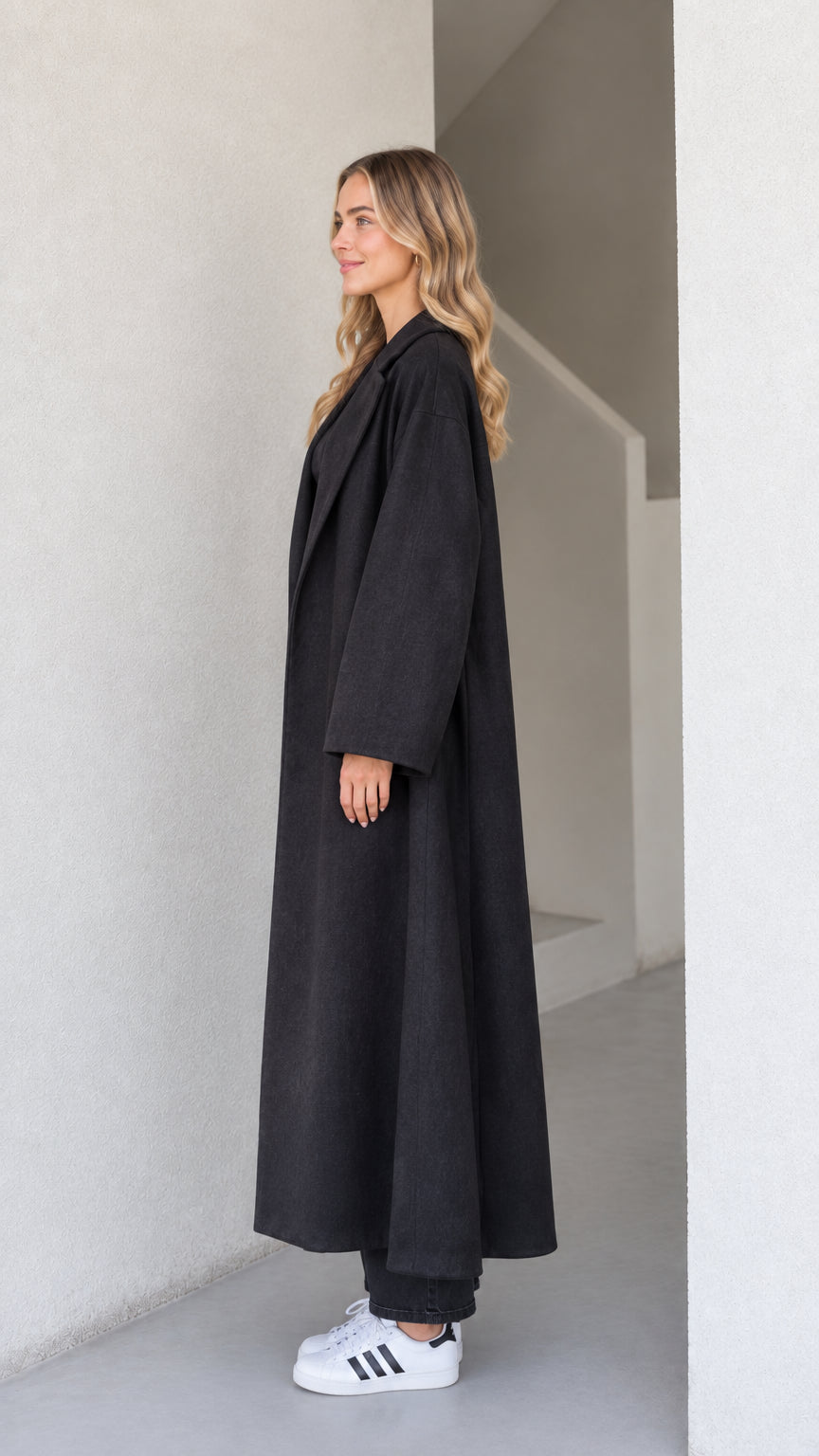 Side profile view of the black oversized floor-length coat showcasing its fluid drape