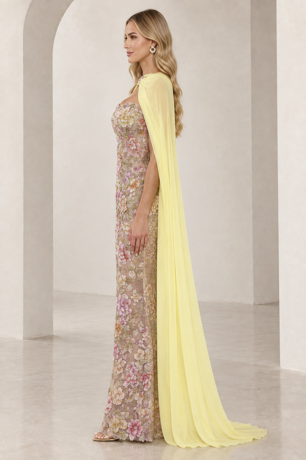 Side profile of model wearing floral embroidered column gown with flowing yellow chiffon cape