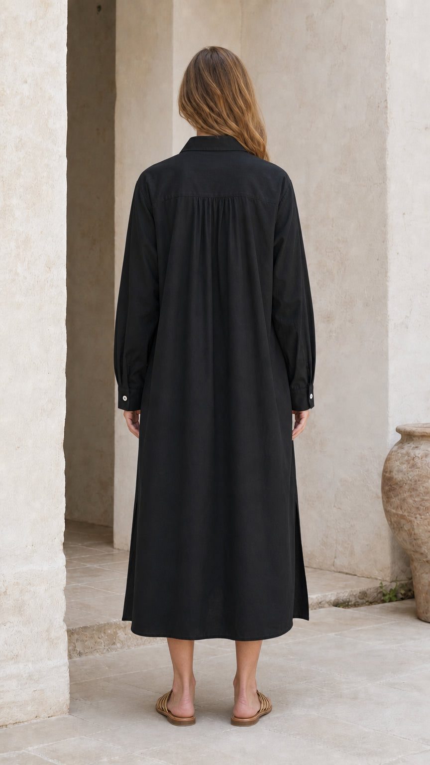 Back view of woman in black long sleeve relaxed midi dress with gathers