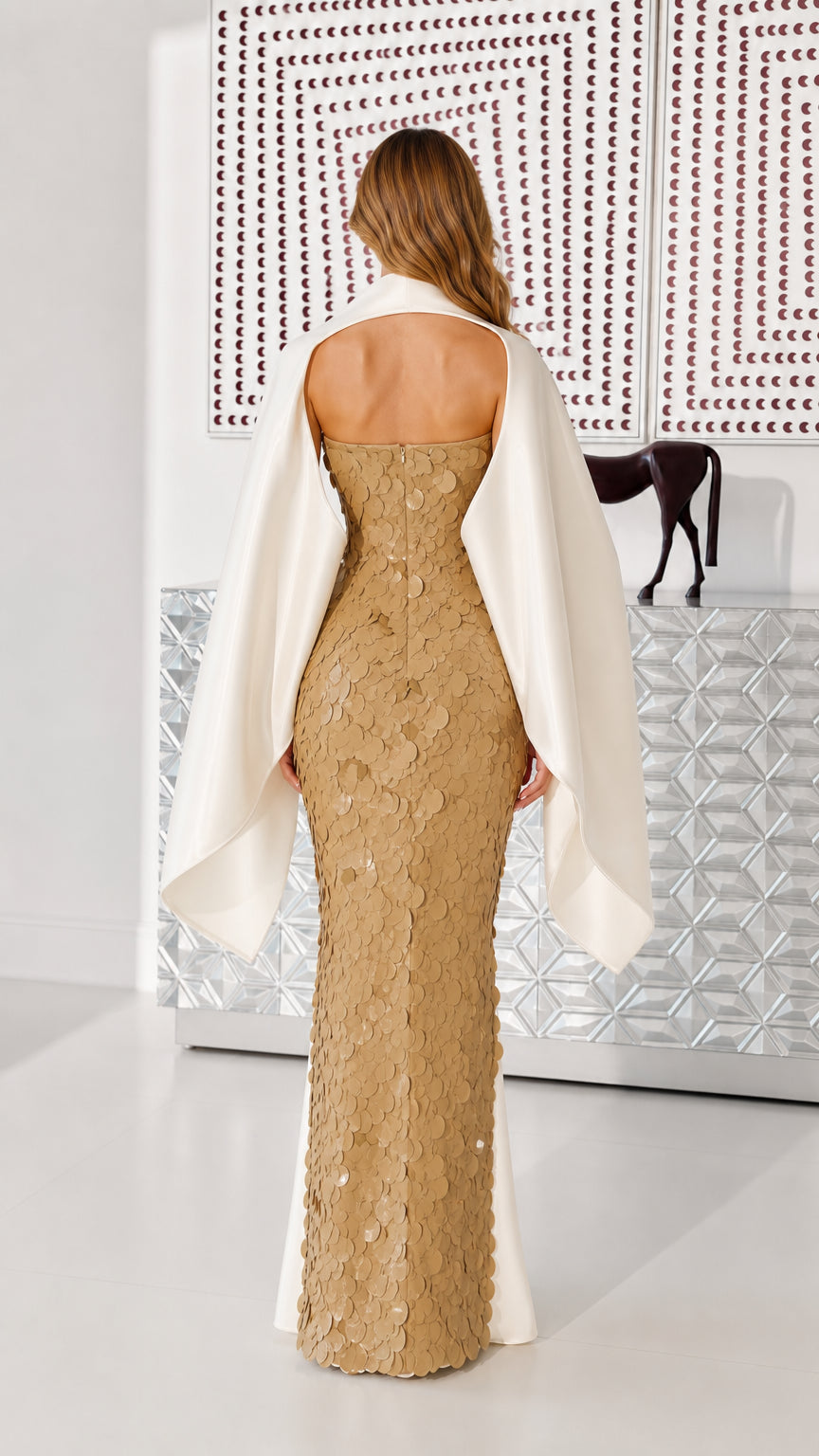 Back view of gold sequin maxi dress showcasing open back and draped cape