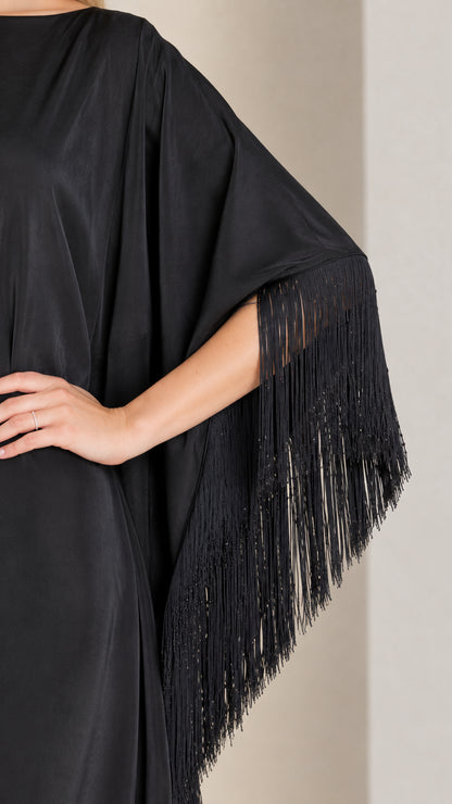Close-up detail of fringe trim on batwing sleeve of black satin dress