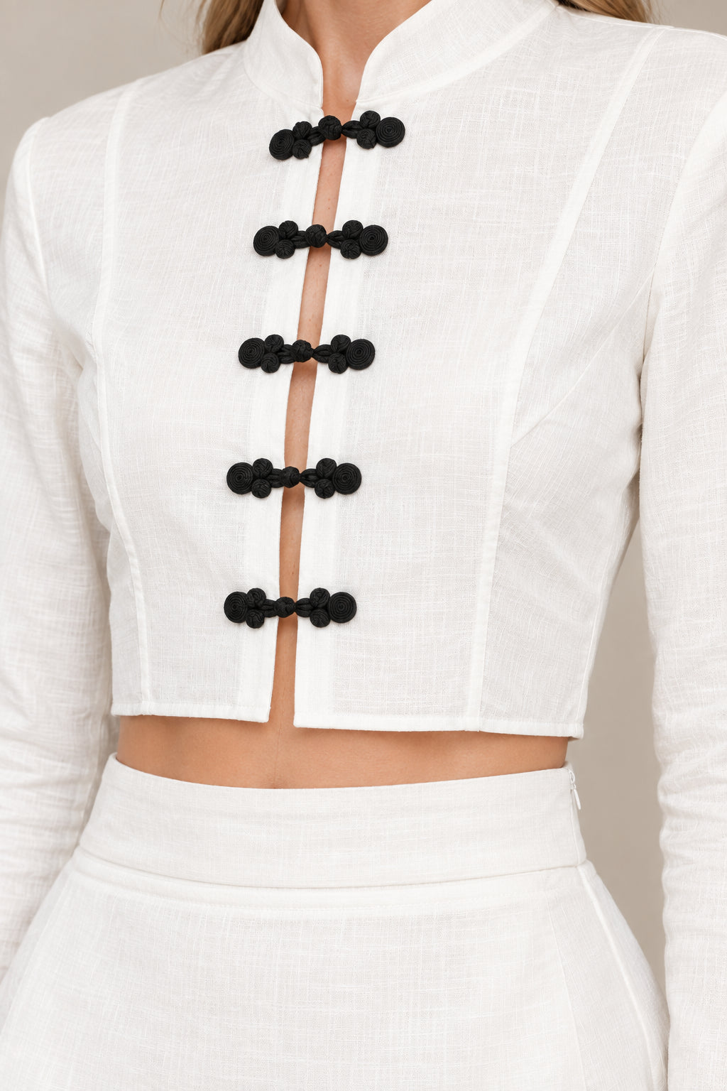 Close-up detail of white mandarin collar crop top with black frog knot buttons