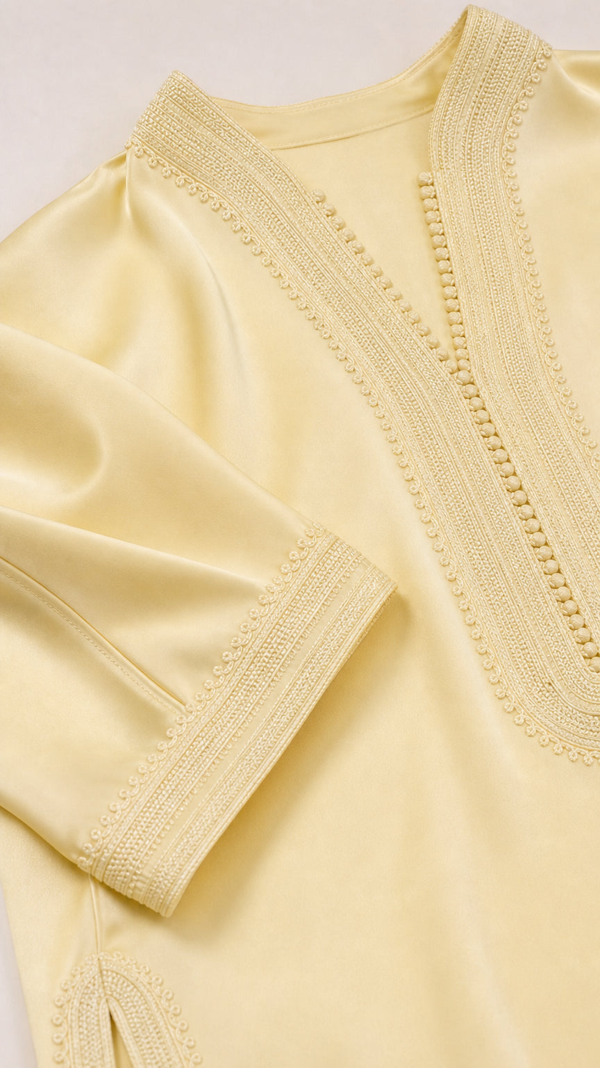 Close-up detail of textured embroidery on neckline and cuff of pastel yellow tunic