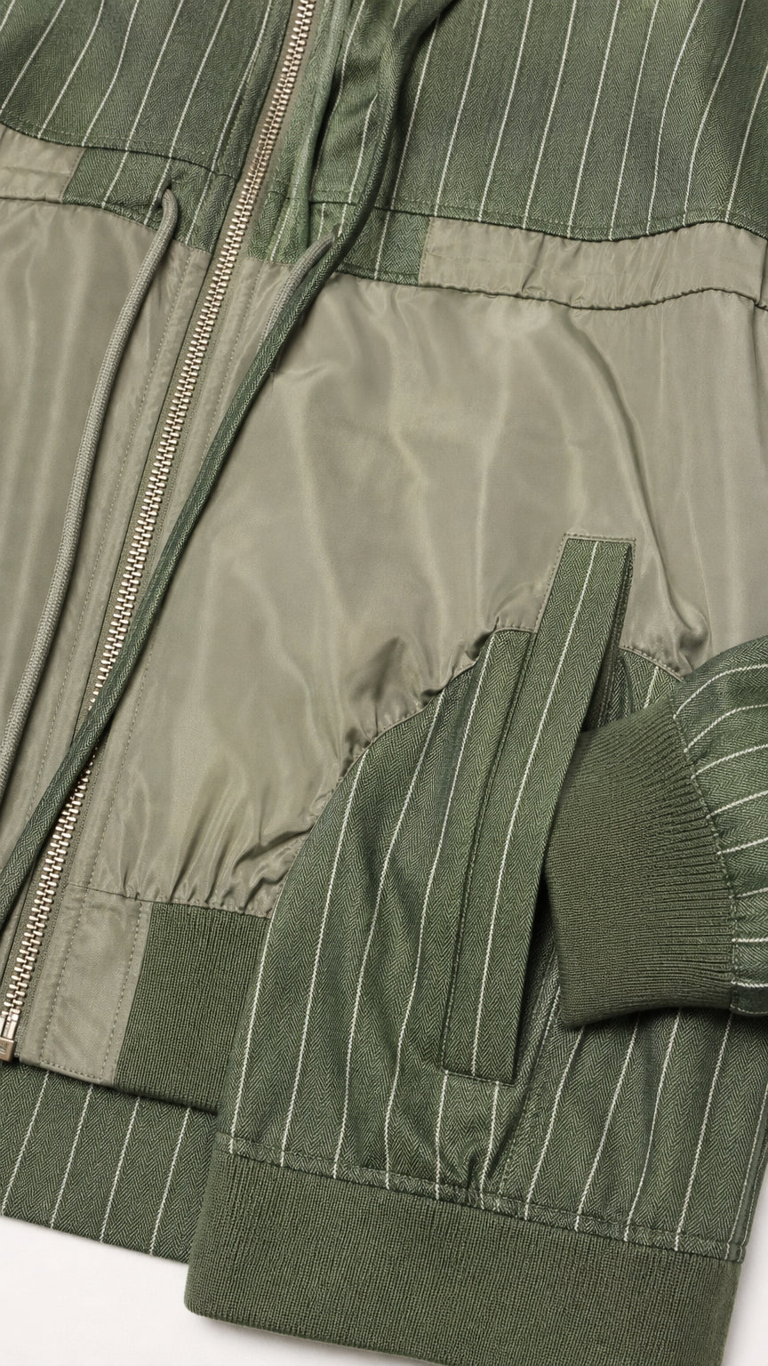 Close-up detail of zipper, ribbed cuffs, and contrast panels on olive green jacket
