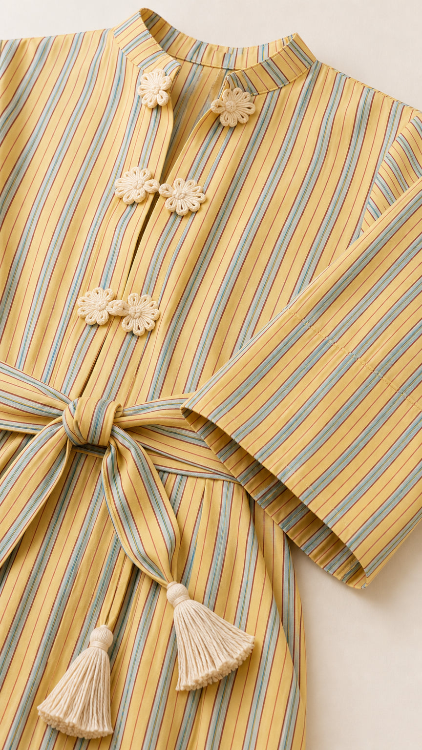 Close-up detail of mandarin collar, knot button closures, and tassel belt on yellow striped dress