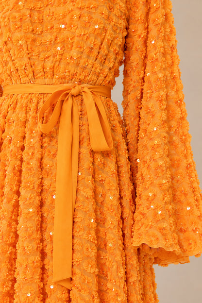Close-up detail of textured fabric, micro sequins, and tie belt in orange