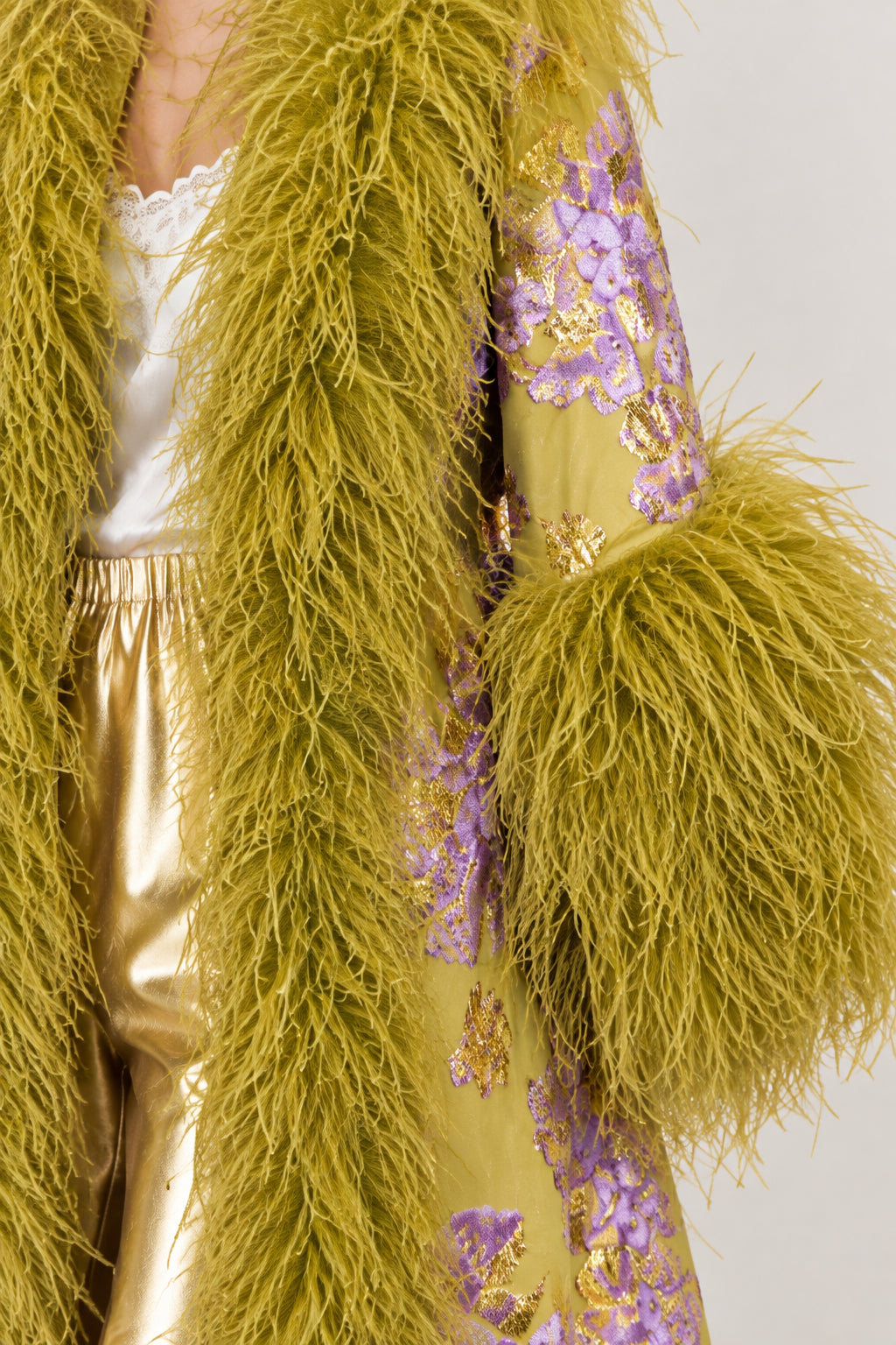 Close-up detail of textured floral jacquard fabric and fluffy feather trim on olive green coat