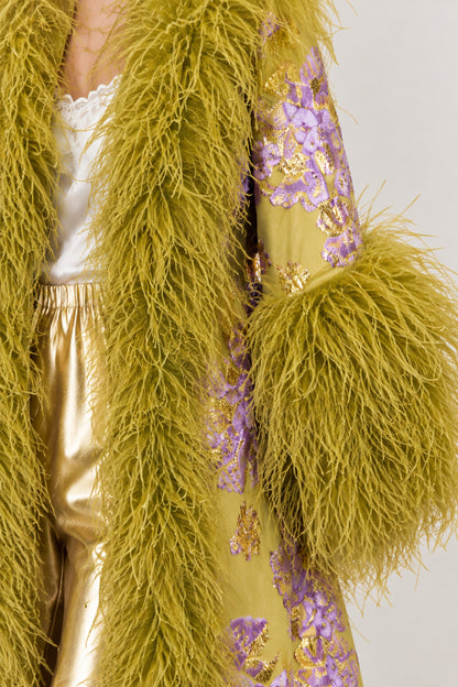 Close-up detail of textured floral jacquard fabric and fluffy feather trim on olive green coat