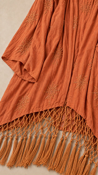 Close-up detail of terracotta textured fabric, sunburst embroidery, and knotted macrame fringe