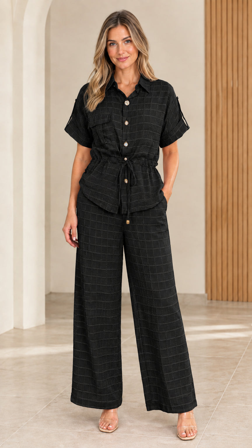 Full front view of model wearing black textured short sleeve shirt and wide leg trousers set