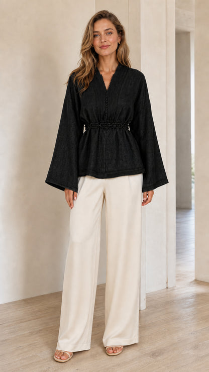 Model wearing black V-neck bell sleeve peplum blouse with wide-leg trousers
