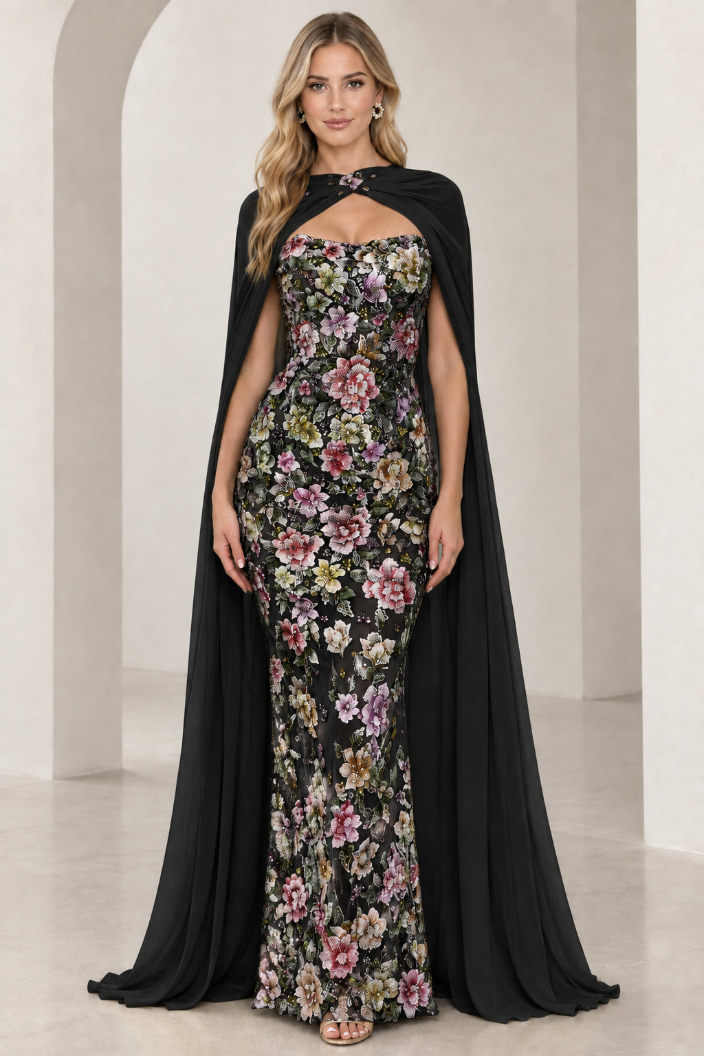 Model wearing black floral embroidered evening gown with full-length black chiffon cape