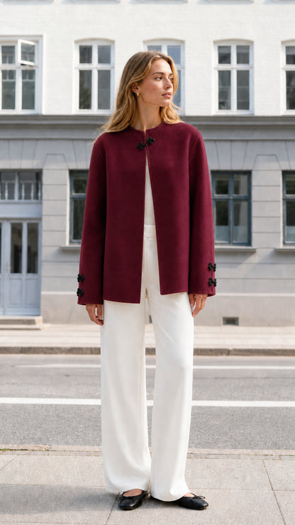Front full view of woman wearing burgundy collarless knot clasp jacket with white trousers