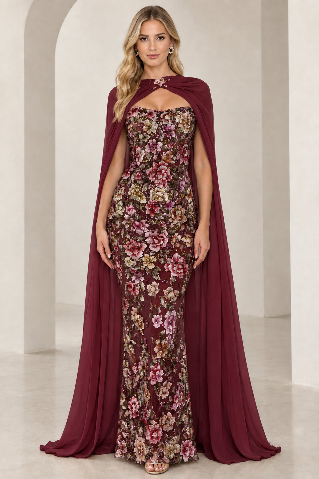 Model wearing rich burgundy wine floral embroidered evening gown with flowing cape